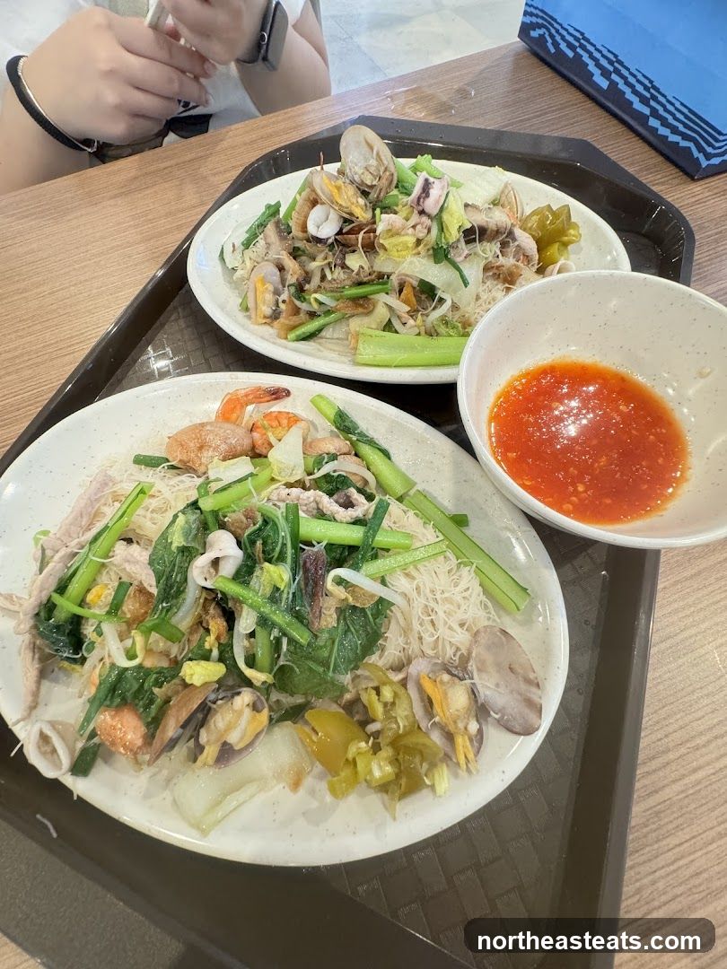 Two plates of stir-fried noodles with seafood and vegetables