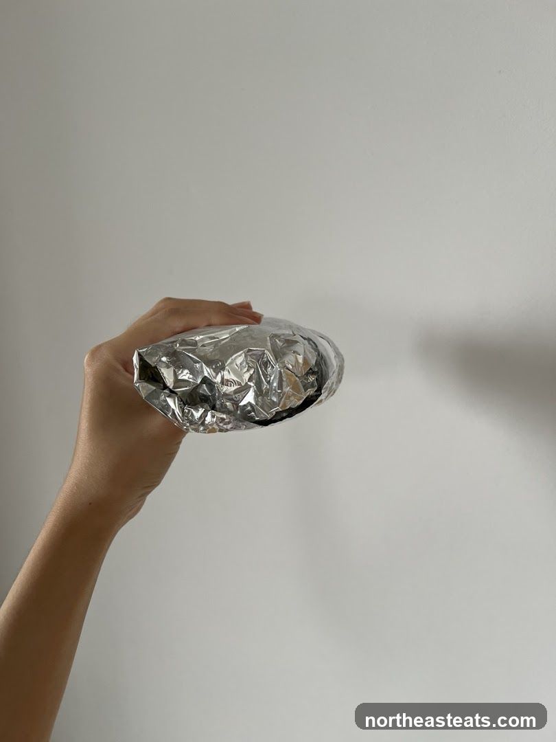 Hand holding a foil-wrapped burrito