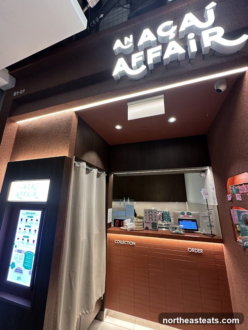 The exterior of a shop with a prominent sign that reads "AN ACAI AFFAIR". To the left, a digital menu board displays various acai bowl and smoothie options. The counter area has signs for "COLLECTION" and "ORDER".