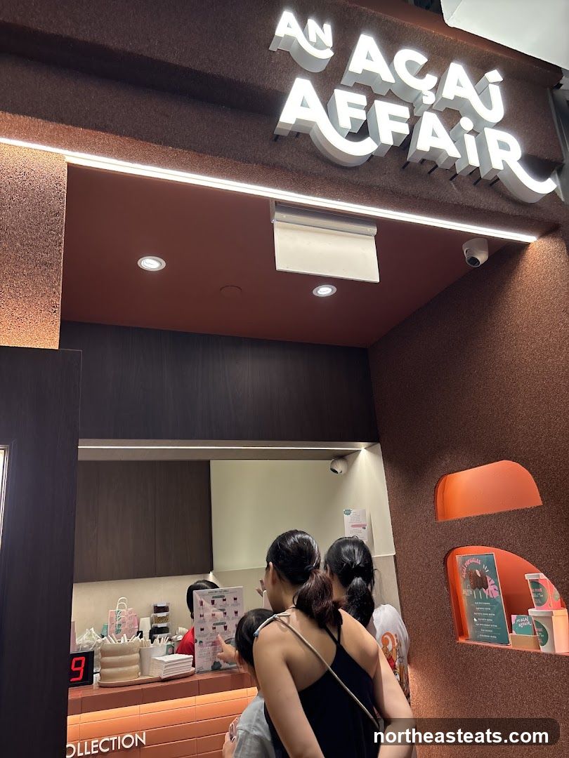 The exterior of an Açaí shop with illuminated signage that reads "AN AÇAÍ AFFAIR". There is a counter area visible inside where customers are queuing.