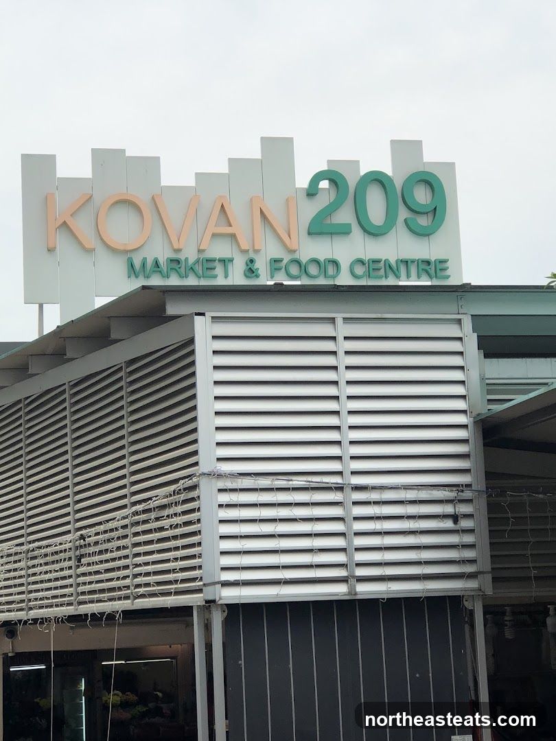 A sign for Kovan 209 Market & Food Centre is visible above the building. The building has louvred panels and some decorative lights.