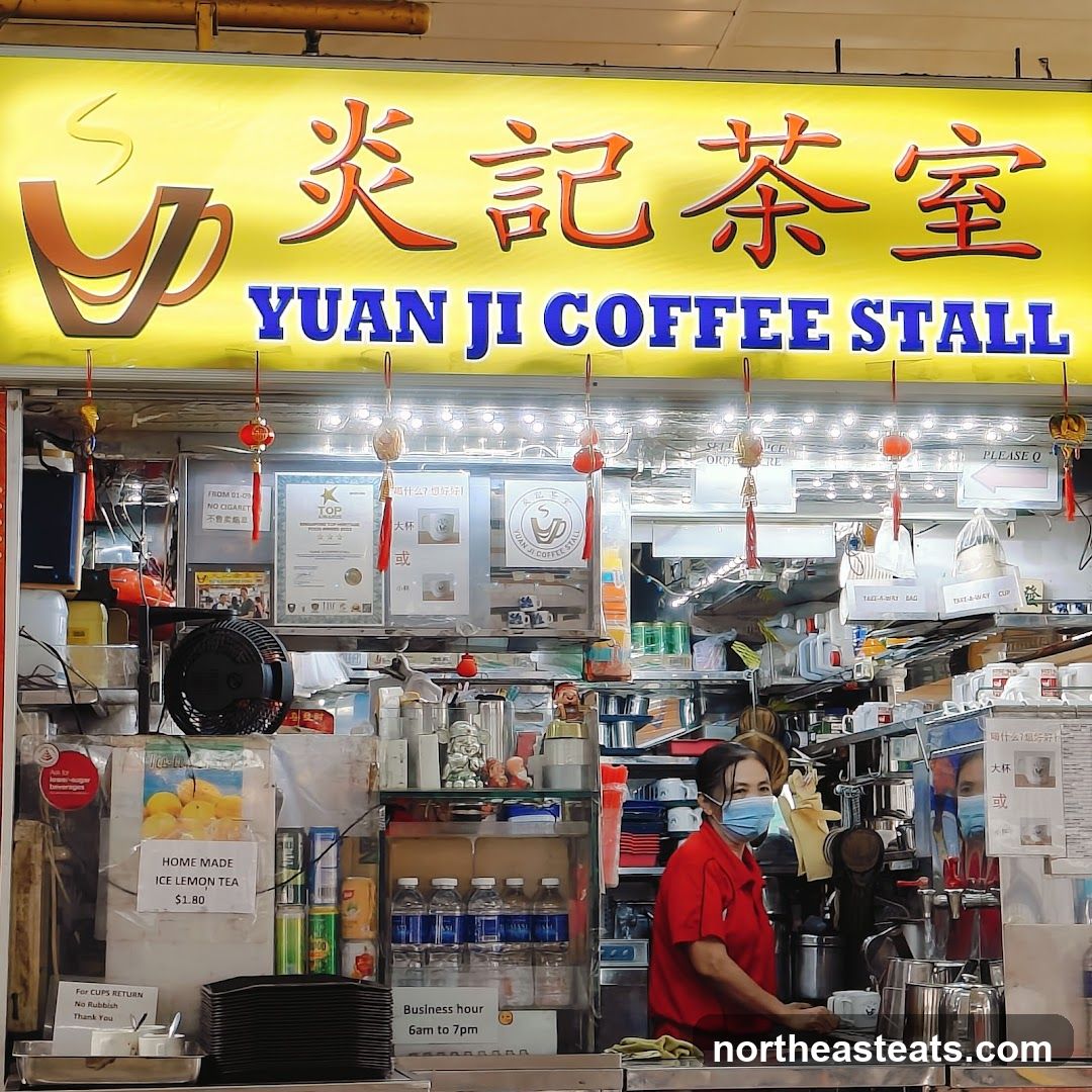 A brightly lit coffee stall with a large yellow sign displaying Chinese characters and the English name "YUAN JI COFFEE STALL". Below the sign, the stall is stocked with drinks, cups, and various items. A woman in a red shirt and face mask is visible behind the counter, preparing drinks. A sign advertises "HOME MADE ICE LEMON TEA $1.80". The business hours are listed as "6am to 7pm".