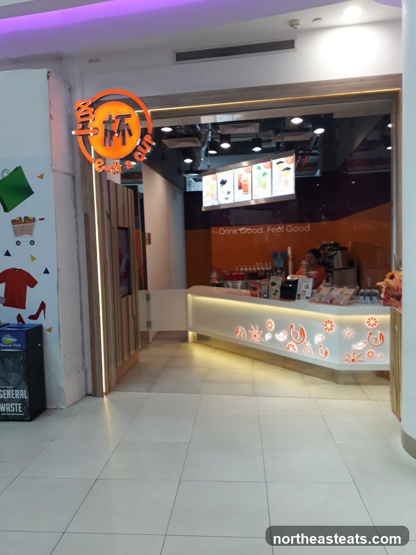 A brightly lit shop front with a prominent orange and white logo above the entrance. Inside, a counter displays various drinks and a menu board. The slogan "Drink Good, Feel Good" is visible.