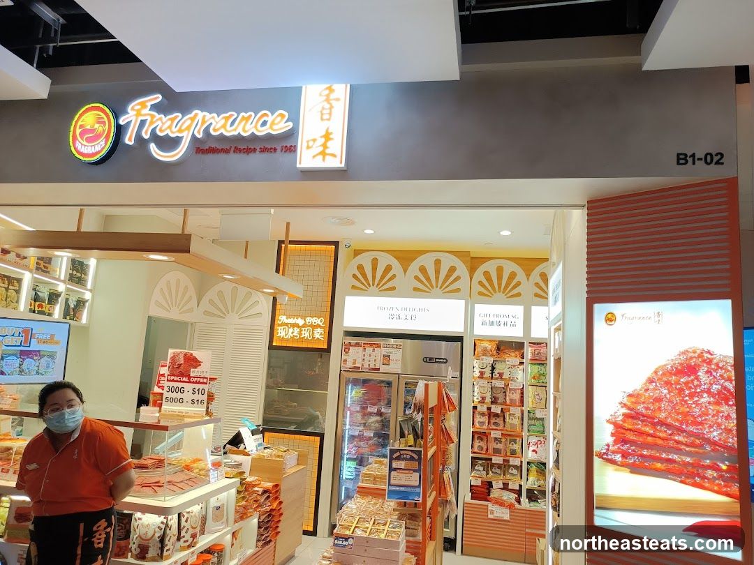 The exterior of a Fragrance shop, a food store specializing in traditional recipes since 1965. The shop has a bright interior with shelves stocked with various food products. A staff member wearing an orange uniform and a face mask stands behind a counter. A prominent sign displays
