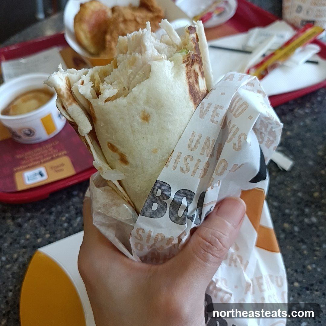 Hand holding a burrito wrapped in branded paper