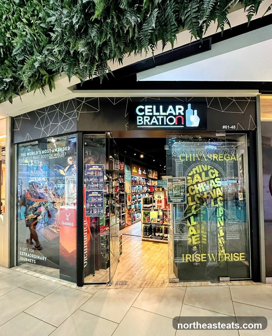 The exterior of a liquor store with a prominent "CELLARBRATION" sign above the entrance. The storefront features large glass windows displaying various bottles of alcohol and promotional materials. A lush green plant installation hangs above the entrance.