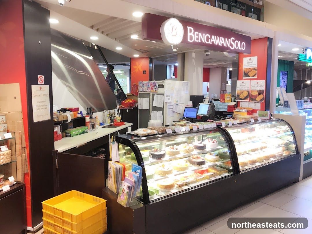 A bakery storefront with a display case filled with cakes and pastries. The shop's name, Bengawan Solo, is visible on a sign above the counter. There is also a "We are Hiring!" sign posted.