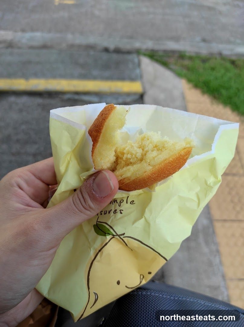 Hand holding a partially eaten pastry in a yellow paper bag
