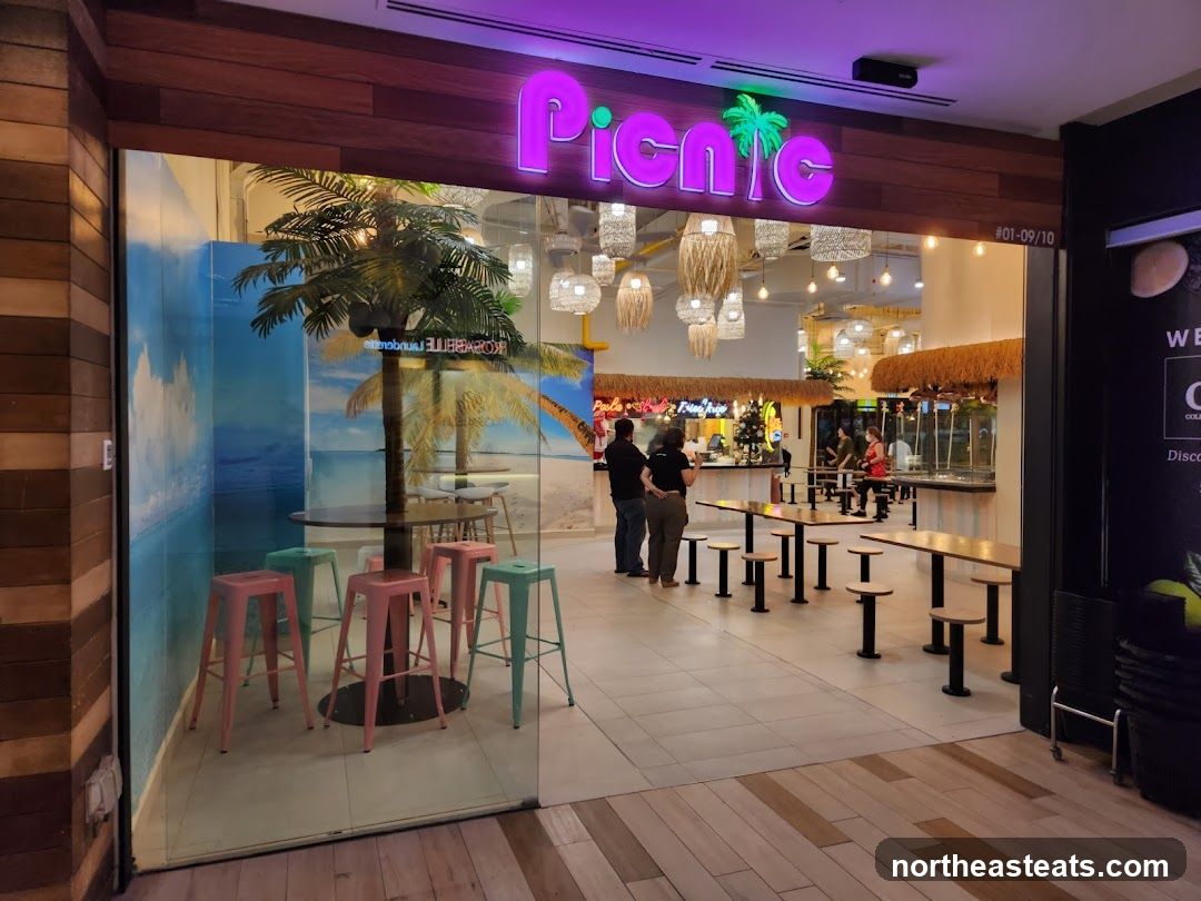 The exterior of a restaurant called Picnic, with a neon sign above the entrance. Inside, there are tables and chairs, and a tropical-themed mural on the wall. Several people are visible inside the restaurant.