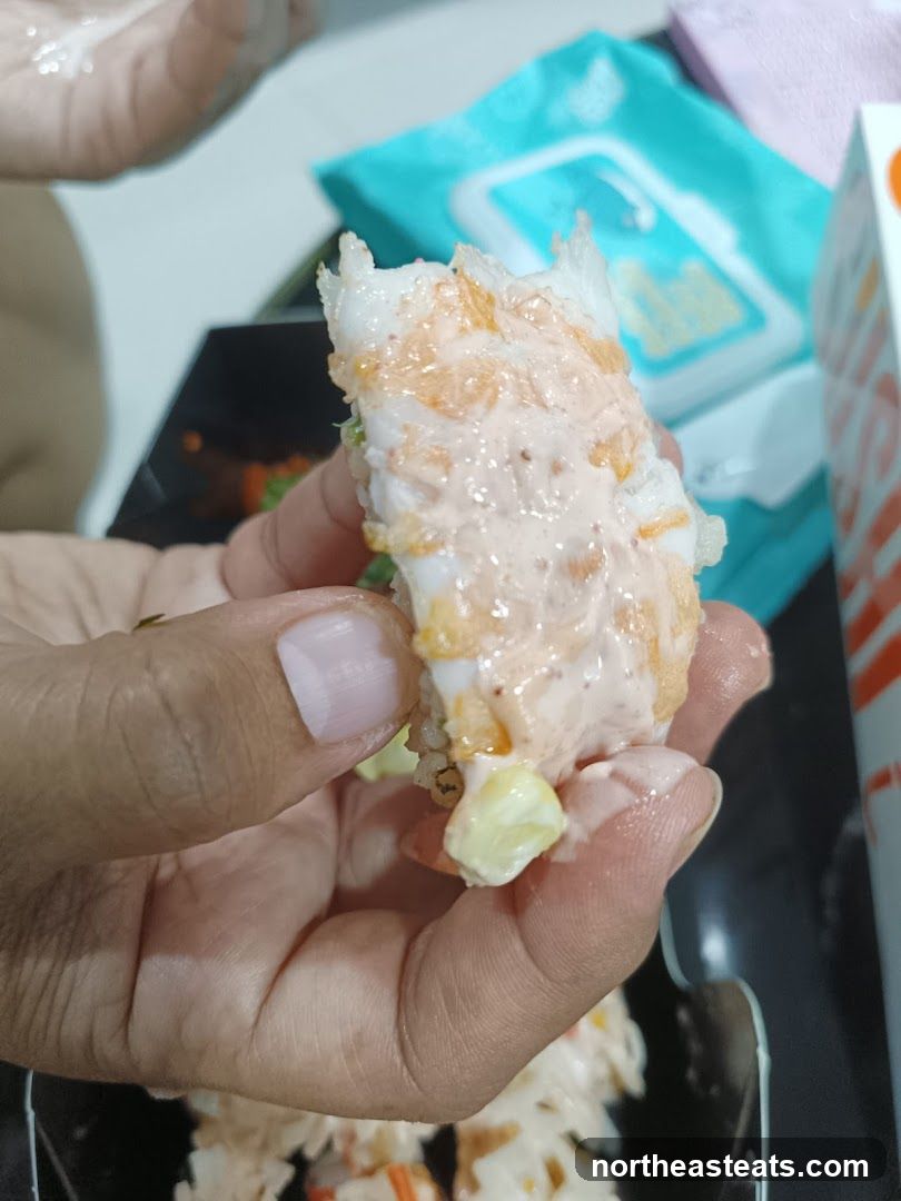 Close-up of a hand holding a piece of sushi with sauce