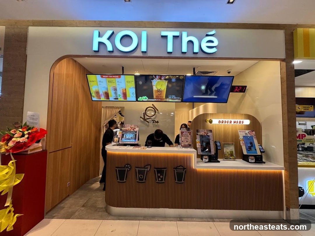 A KOI Thé shop front with a prominent sign above the entrance. The counter area displays digital menus and ordering kiosks. Staff members are visible behind the counter.