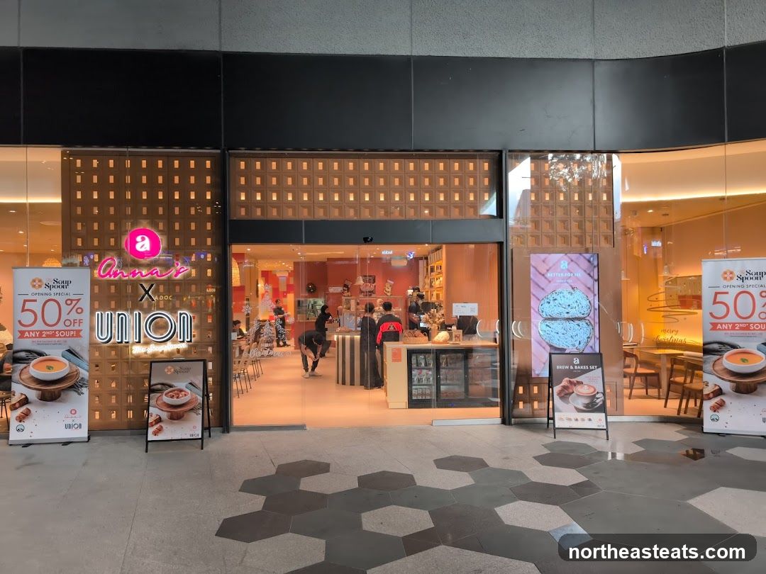 The exterior of a shop called Anna's Union. There are promotional banners outside the shop advertising a 50% off opening special on any 2nd soup. Inside, the shop is brightly lit with orange accents and displays food and drinks.