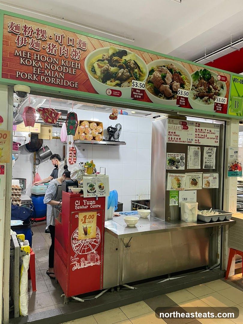 A hawker stall with a large sign displaying images and names of noodle dishes and pork porridge. The stall has a counter with bowls and utensils, and staff members are visible preparing food in the background. A red cooler with the text "Ci Yuan Hawker Centre" and a Ferris wheel graphic is also present.