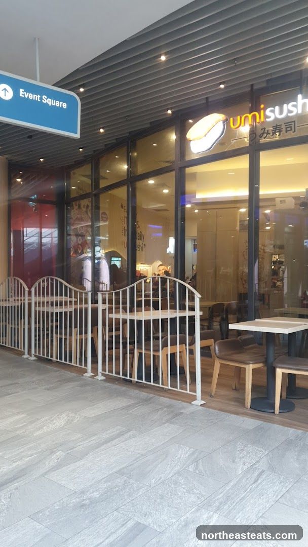 The exterior of a Umi Sushi restaurant with large glass windows and a white railing enclosing an outdoor seating area. The restaurant's logo and name are visible on the facade.