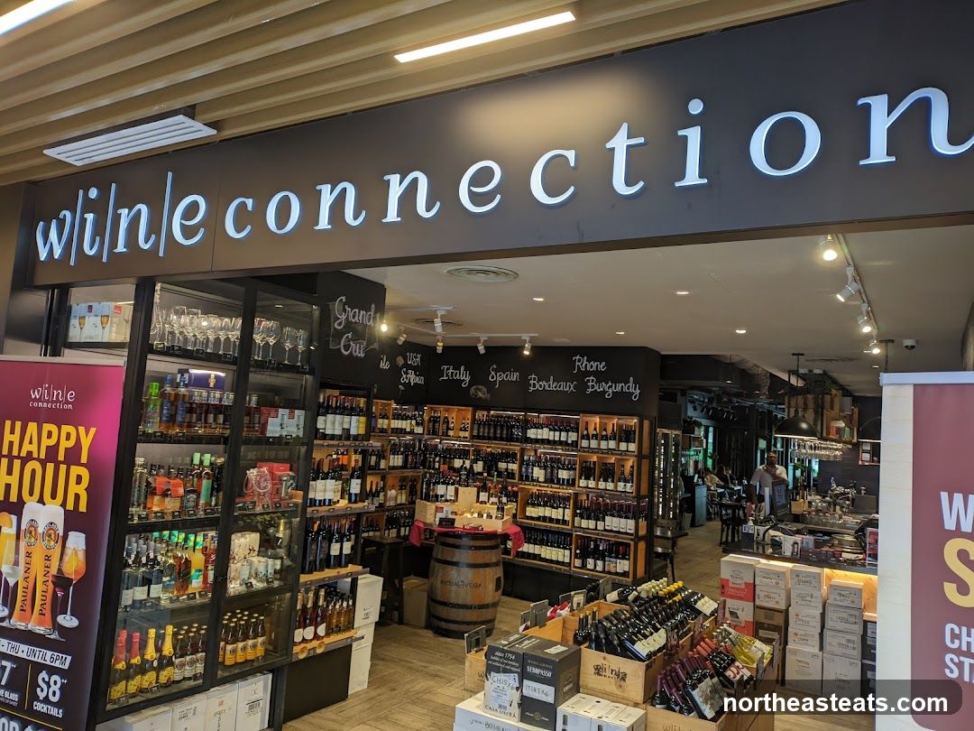 The exterior of a wine shop with a large sign that reads "wine connection". The shop displays a wide selection of wine bottles and glasses. There is also a "Happy Hour" promotion visible.