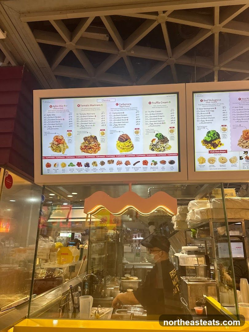 A digital menu board displaying various pasta dishes with toppings.