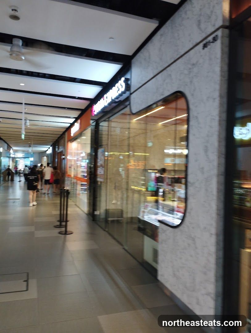 A view down a modern, well-lit shopping arcade with several storefronts. The focus is on a store with a prominent illuminated sign that reads "EXPRESS". The facade features large glass windows, allowing a glimpse into the interior, which appears to be a retail space with displays. The exterior wall of the adjacent unit is textured with a grey, marble-like pattern.