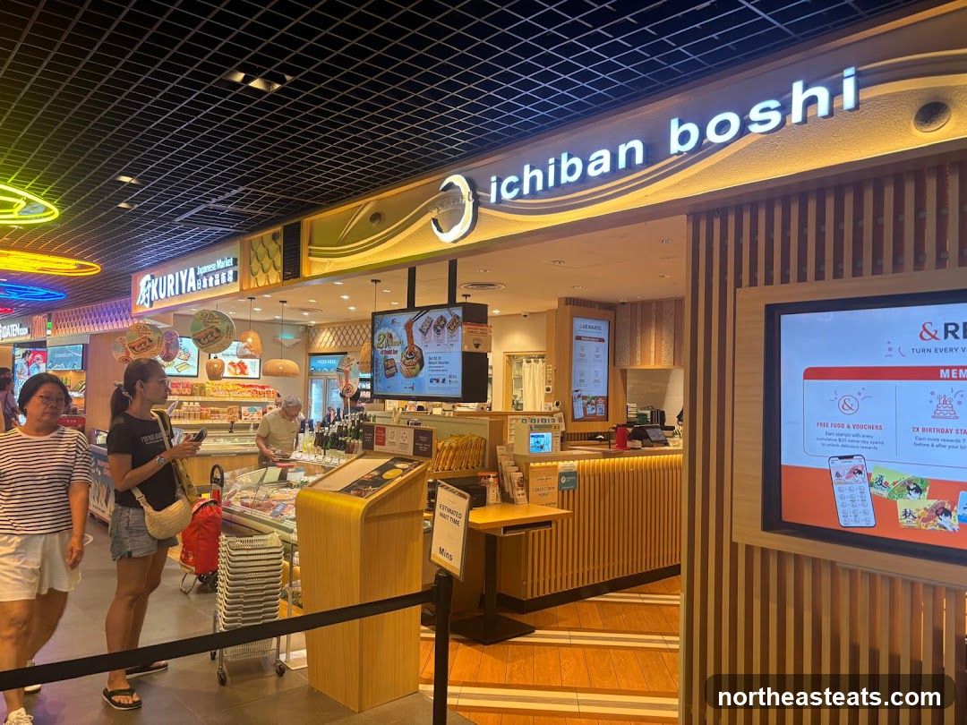 The exterior of a Japanese market and restaurant called Ichiban Boshi. The storefront features a prominent sign with the restaurant's name. Inside, there are displays of food products and a counter area. A large screen displays promotional information.