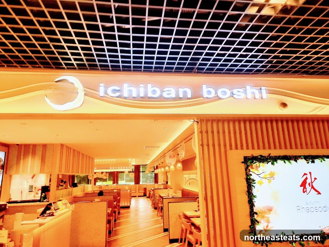 The exterior of a restaurant with the name "ichiban boshi" displayed prominently above the entrance. The interior of the restaurant is visible, showing dining tables and booths. A digital display on the right shows the word "Autumn" and "Rhapsody" with Japanese characters.