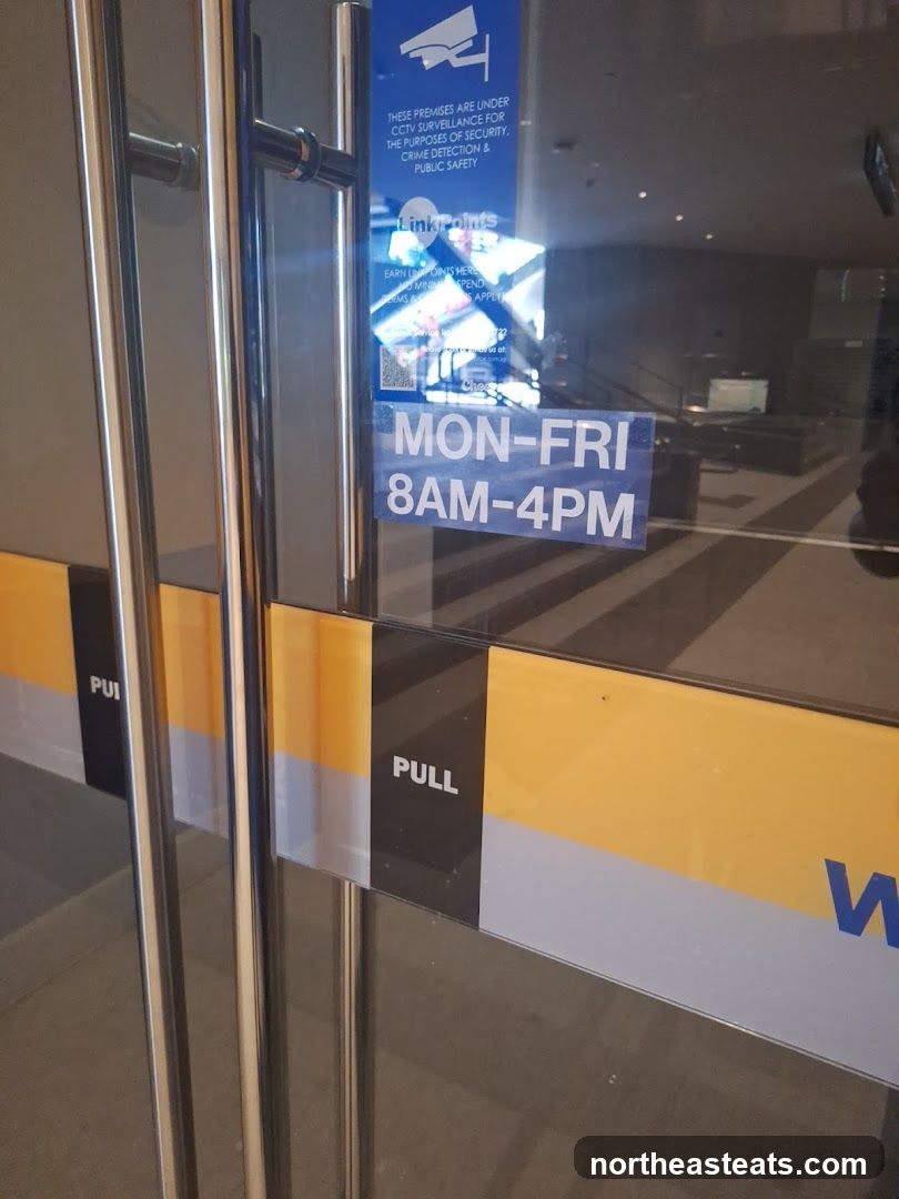 A close-up view of glass doors with metal handles. A blue sticker on the glass indicates that the premises are under CCTV surveillance for security, crime detection, and public safety. It also mentions "Linkpoints" and provides operating hours: Monday-Friday, 8 AM to 4 PM. A yellow and black stripe with the word "PULL" is visible on the lower part of the door.