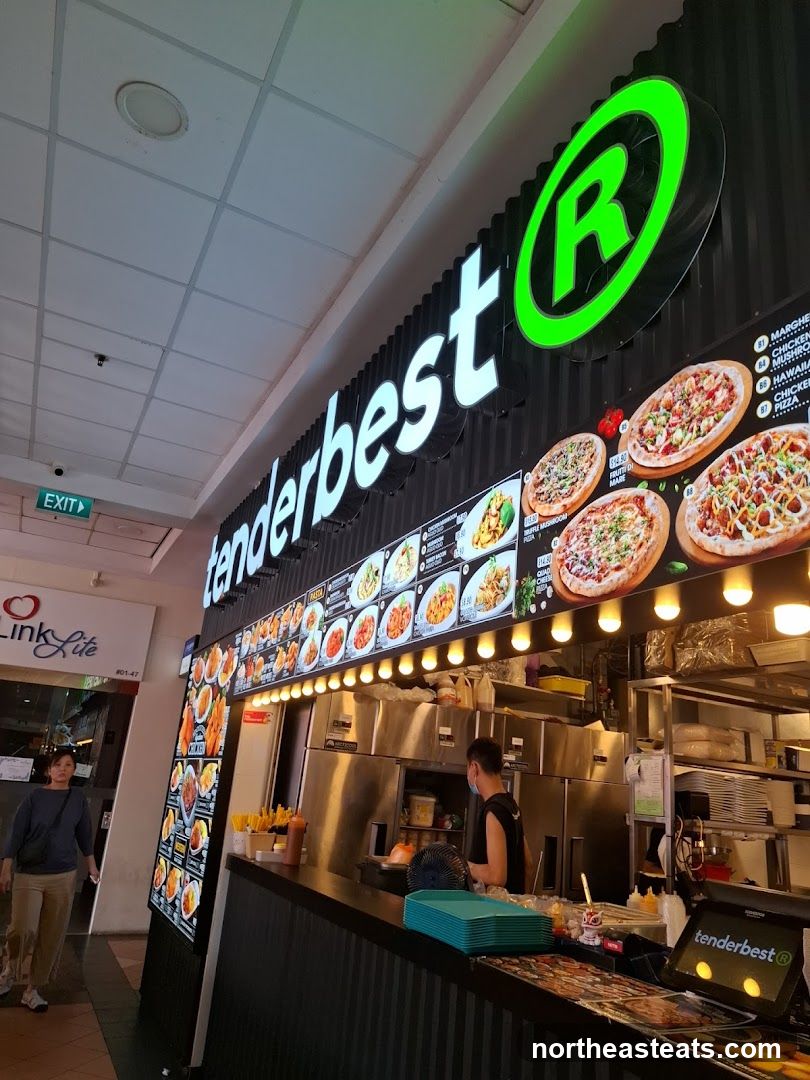 A brightly lit restaurant storefront with a large illuminated sign that reads "tenderbest" and a green circular logo with an "R" inside. Below the sign is a menu display featuring various food items, including pizzas and pasta dishes. A staff member is visible behind the counter, and customers are walking by outside.