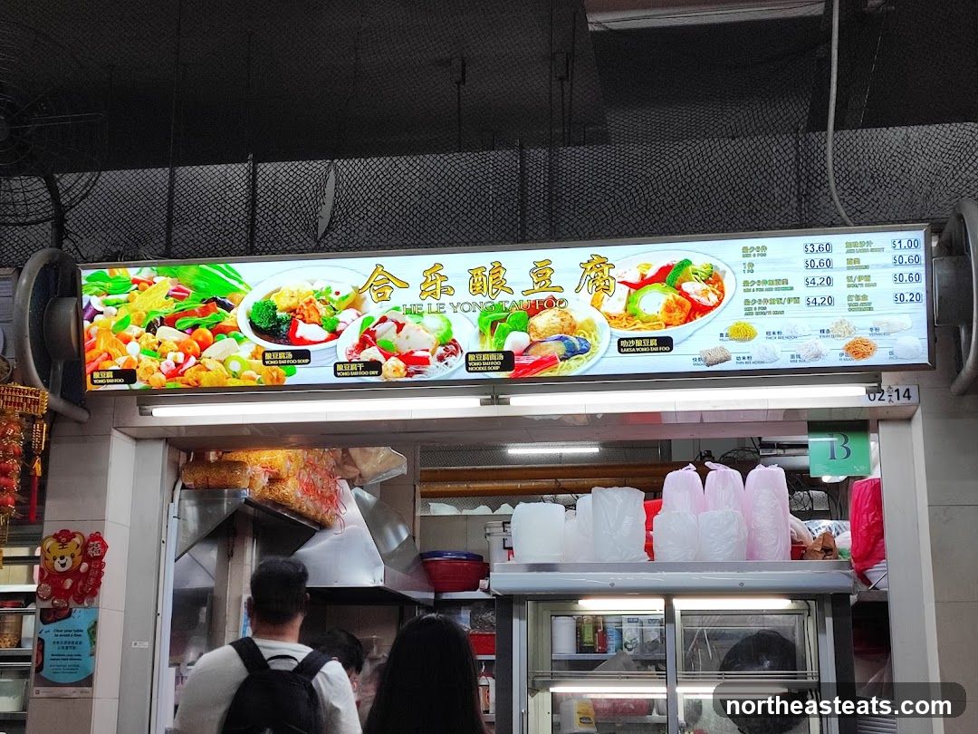 A brightly lit menu board displaying various Yong Tau Foo dishes and noodle options with prices.