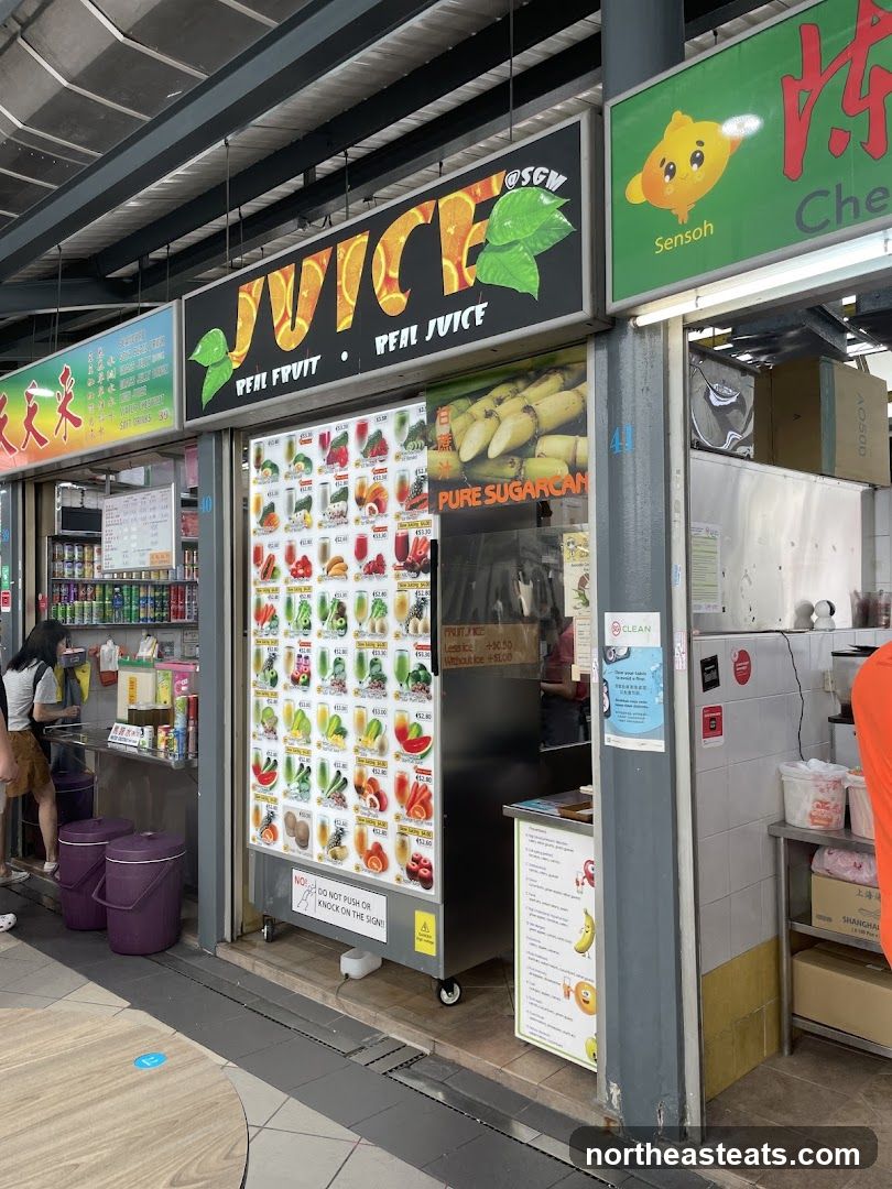 A juice stand with a large sign that says "JUICE REAL FRUIT REAL JUICE". Below the sign is a display of various fruit juices with prices. There is also a sign for "PURE SUGARCAN".