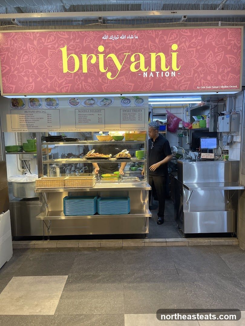 A food stall with a large pink sign featuring the words "briyan NATION" in yellow. Below the sign is a menu board displaying various dishes and prices. A staff member is visible behind the counter.