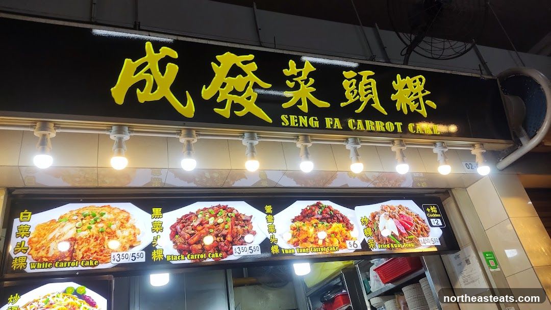 A storefront with a black sign featuring yellow Chinese characters and the English text "SENG FA CARROT CAKE". Below the sign are illuminated menu displays showing various carrot cake dishes and other food items with prices.