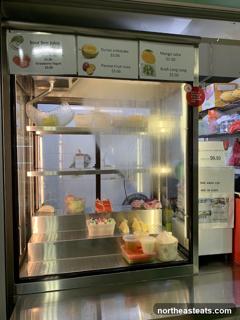 A refrigerated display case filled with various drinks and food items. Above the display are signs listing juice and yogurt options with prices.